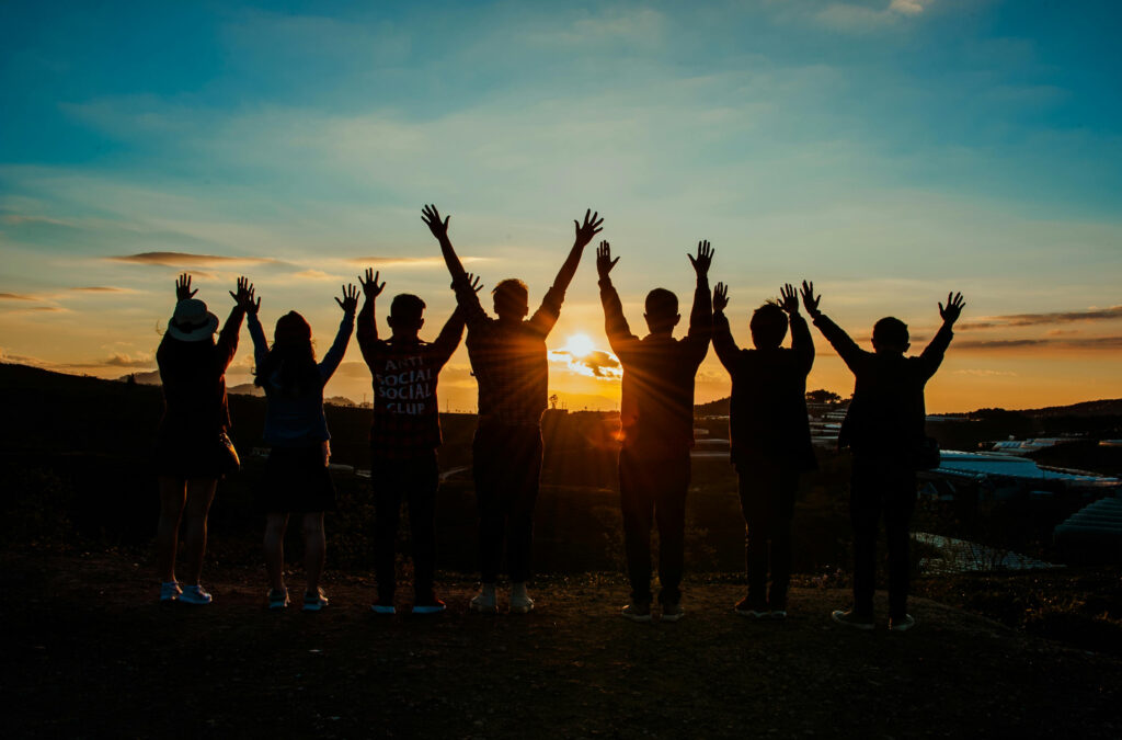 Group of people raising hands together at sunset, representing community, support, and addiction recovery at San Diego Wellness Center.