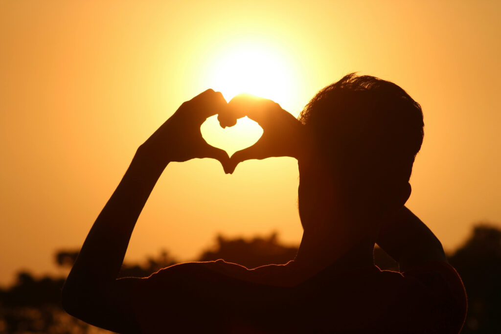 Person holding their hands up forming a heart at sunrise by the ocean, symbolizing hope and recovery at San Diego Wellness Center.