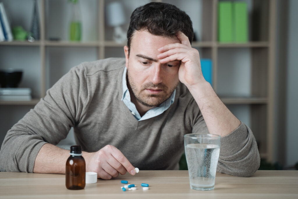 Man looks distressed while holding a pill beside a glass of water, representing benzodiazepine dependence.