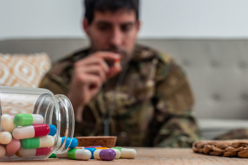 Man sits with prescription pills spilled from a jar, representing PTSD and addiction and the risk of substance misuse.