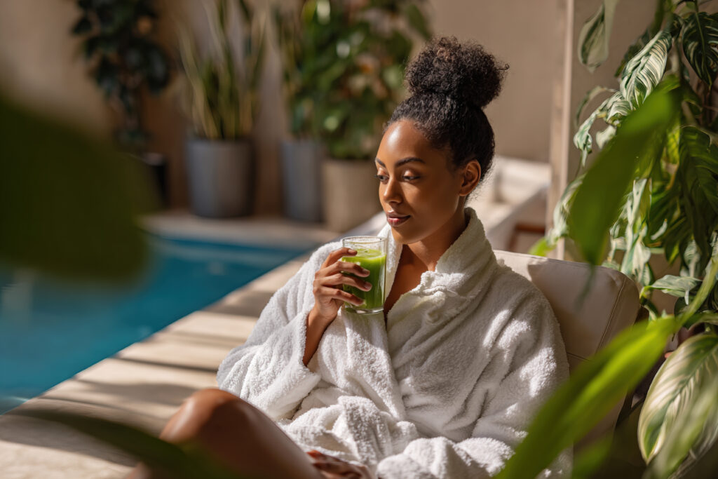 Woman relaxes in a robe by a pool at a luxury rehab in San Diego, holding a healthy green drink.