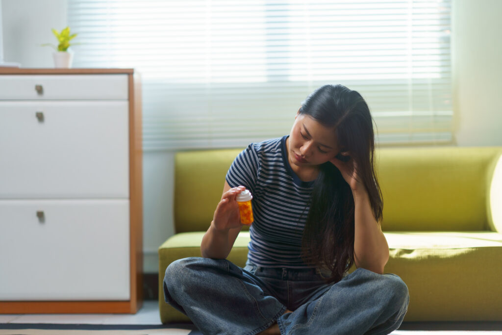 Person holding a prescription pill bottle while experiencing opioid withdrawal symptoms and considering treatment.
