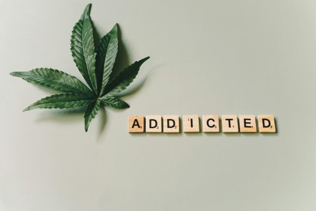 Cannabis leaf beside letter tiles spelling “addicted,” representing laced weed addiction and substance use risks.