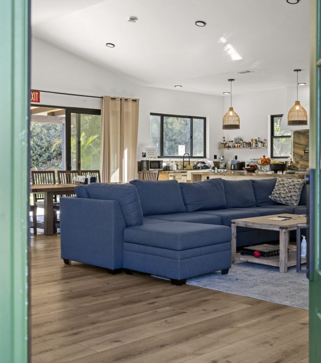 Luxurious living room of the SD-Wellness Drug Rehab Facility in Ironwood, CA. Blue couch with a modern gray rug. Living space displays a modern boho design peeping through a green front door with windows